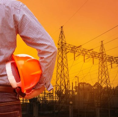 engineer holding yellow safety helmet with electricians working on pylon construction tower in construction site